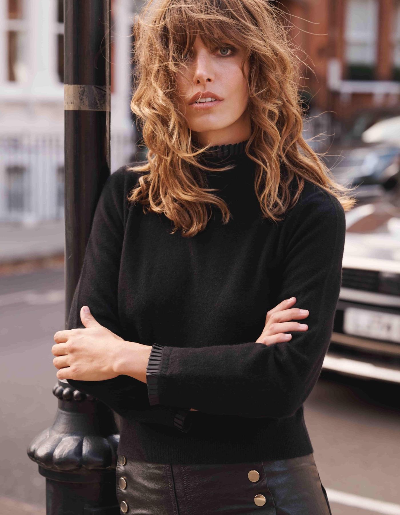 Woman wearing a black pleated neck cashmere sweater standing on a street.