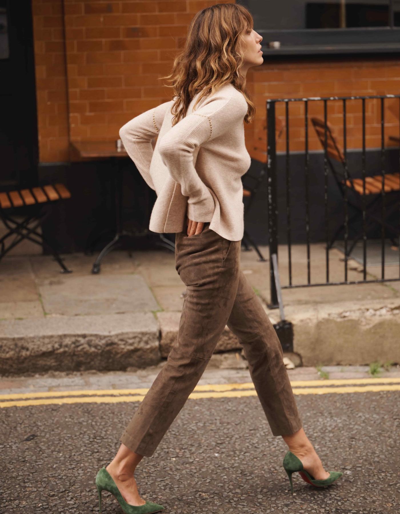 Woman walking on a street wearing a beige cashmere sweater and brown pants.