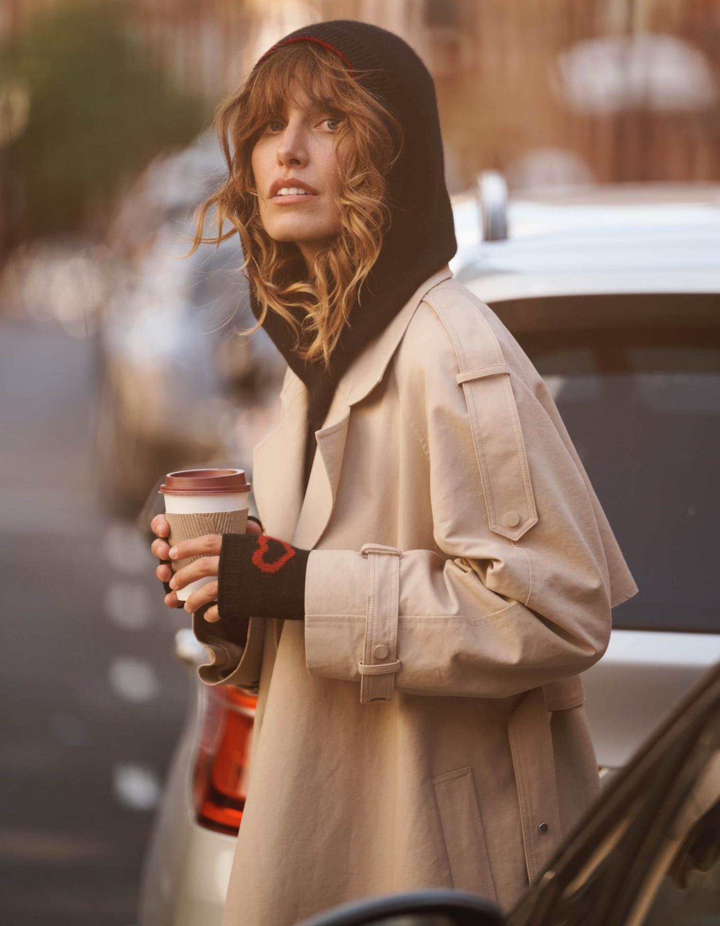 Woman wearing a black cashmere balaklava and gloves holding a take away coffee in her hands in the streets