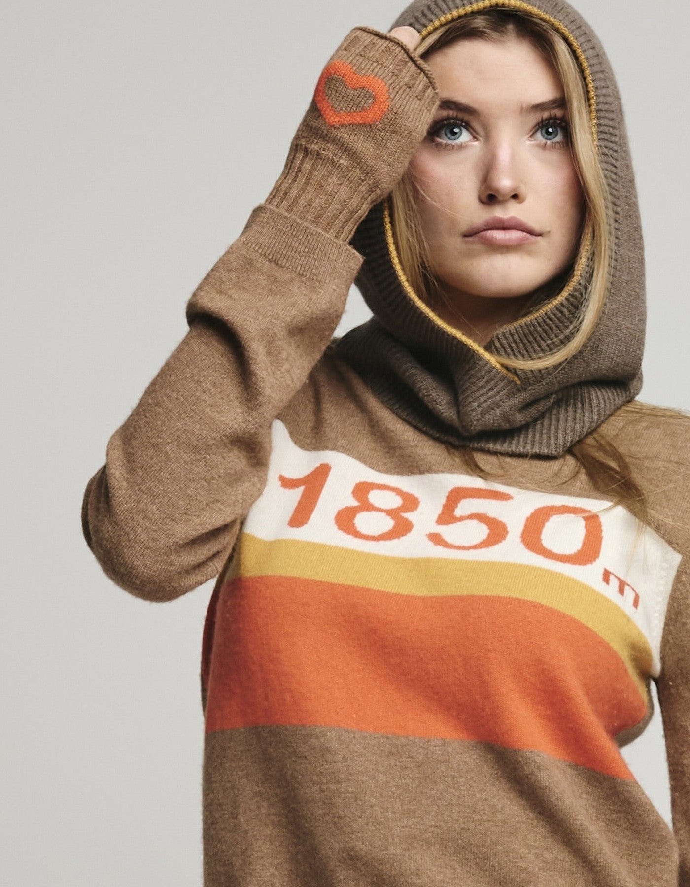 Person wearing a brown sweater with '1850' print, wearing matching balaklava and gloves with hearts on them.