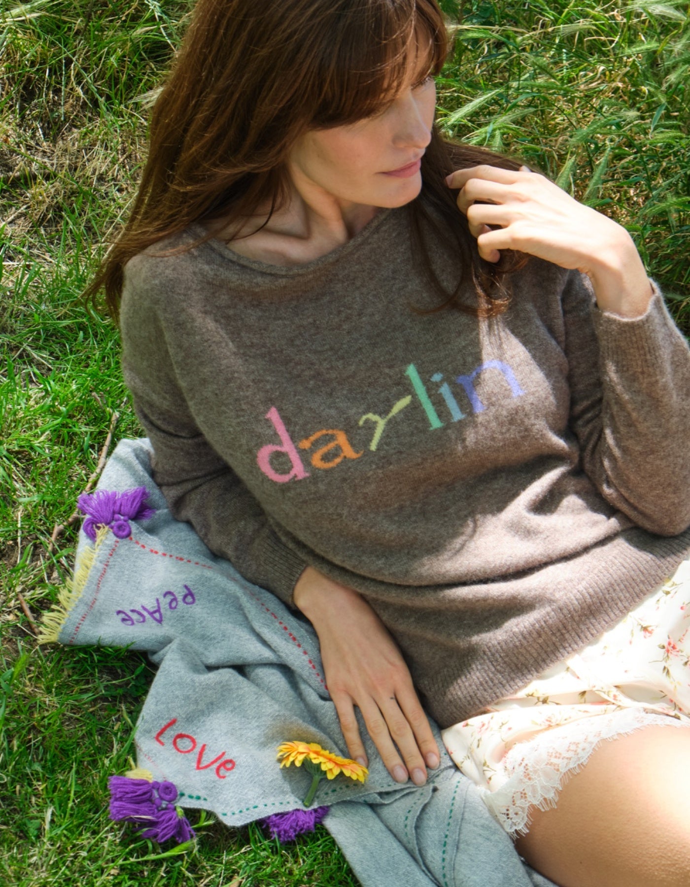 Woman wearing a sweater with 'darlin' in colorful letters, sitting on grass.