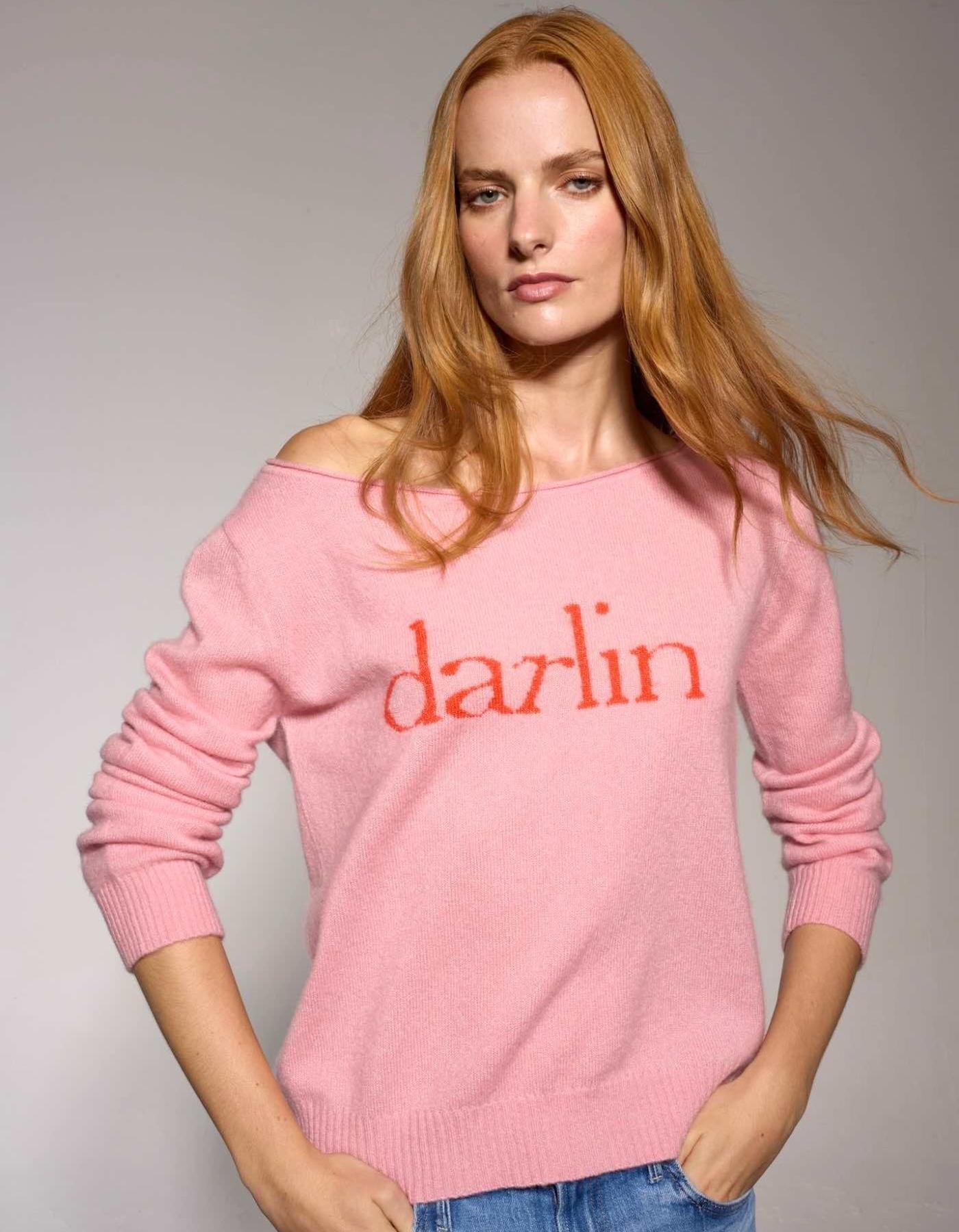 Woman wearing a pink sweater with 'darlin' text on a plain background