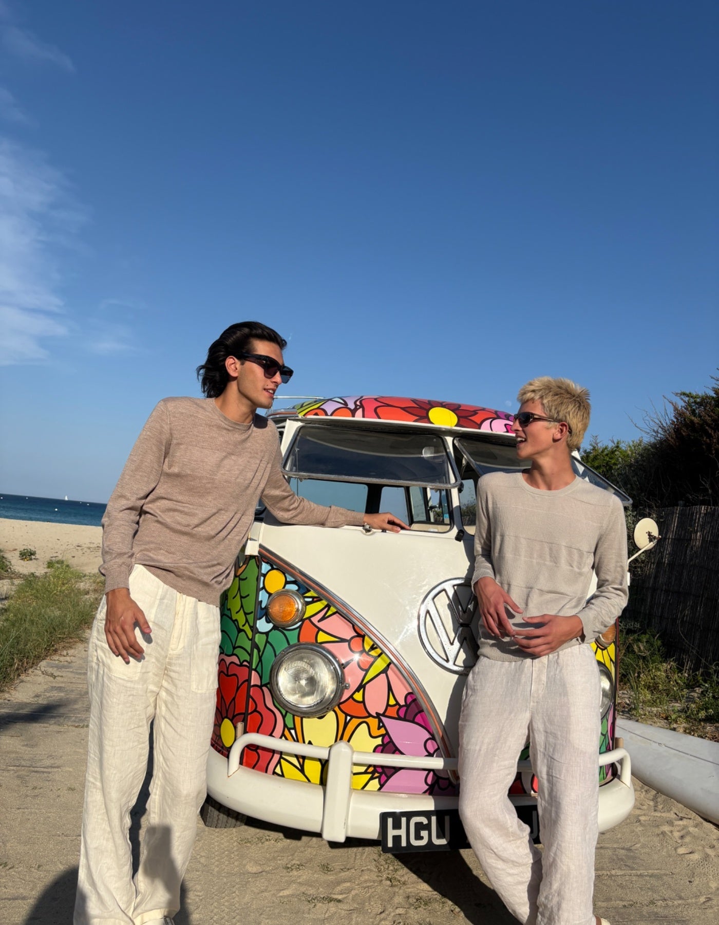 Two people standing next to a colorful Volkswagen van on a beach.