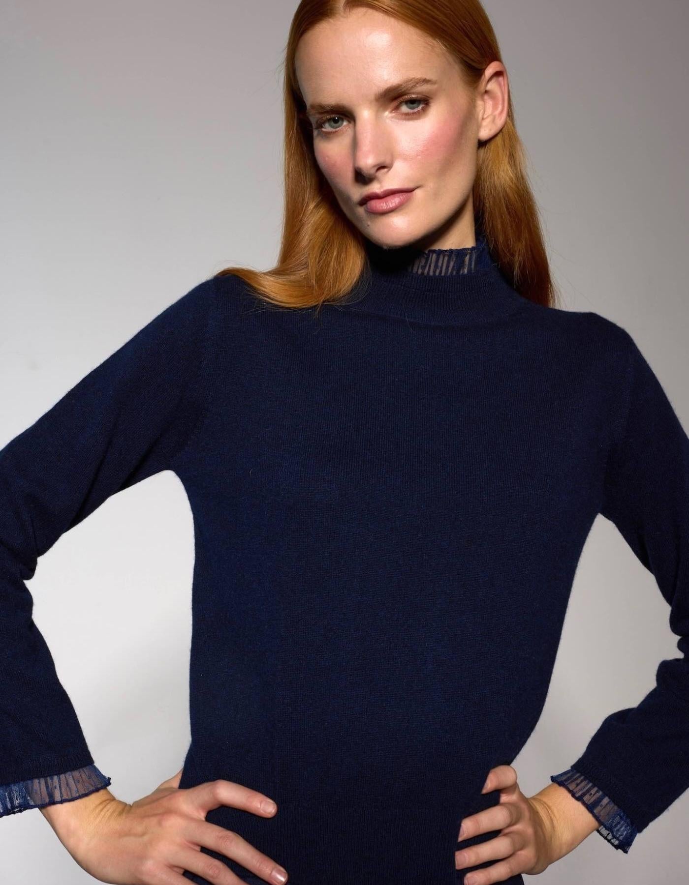 Woman wearing a navy blue lace trim turtleneck sweater against a gray background