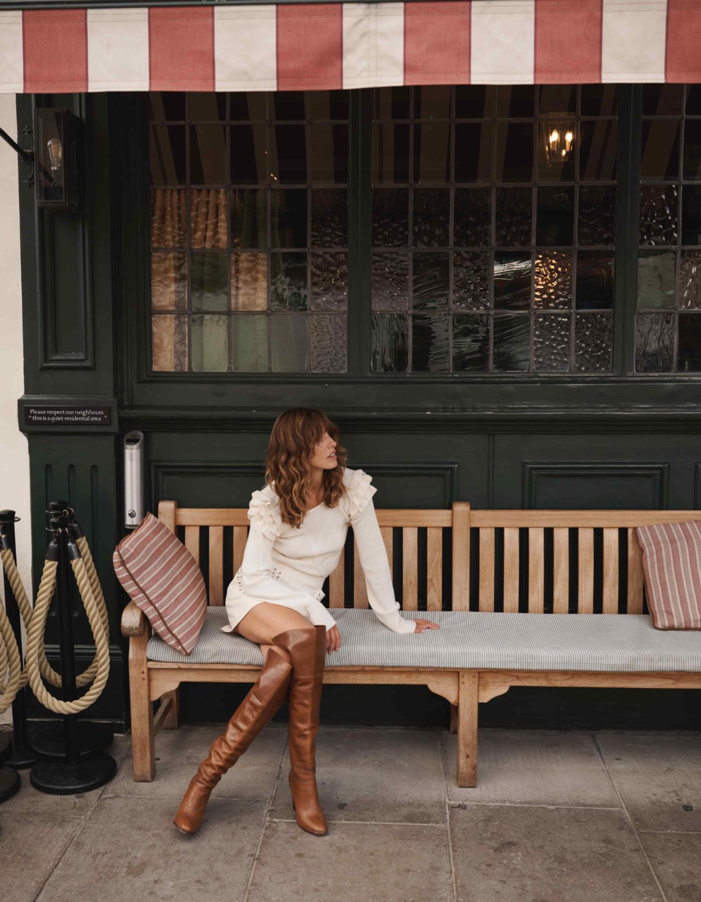 Woman wearing cream cashmere jumper with ruffled shoulders sitting outside pub