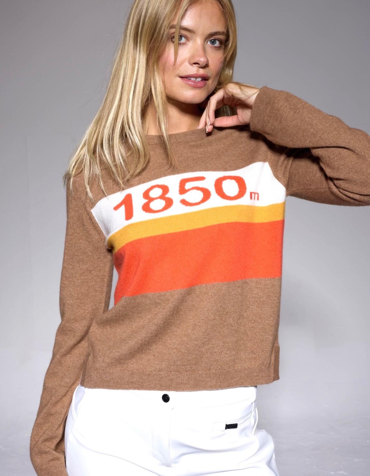 Woman wearing a beige sweater with a colorful logo saying 1850m on a gray background
