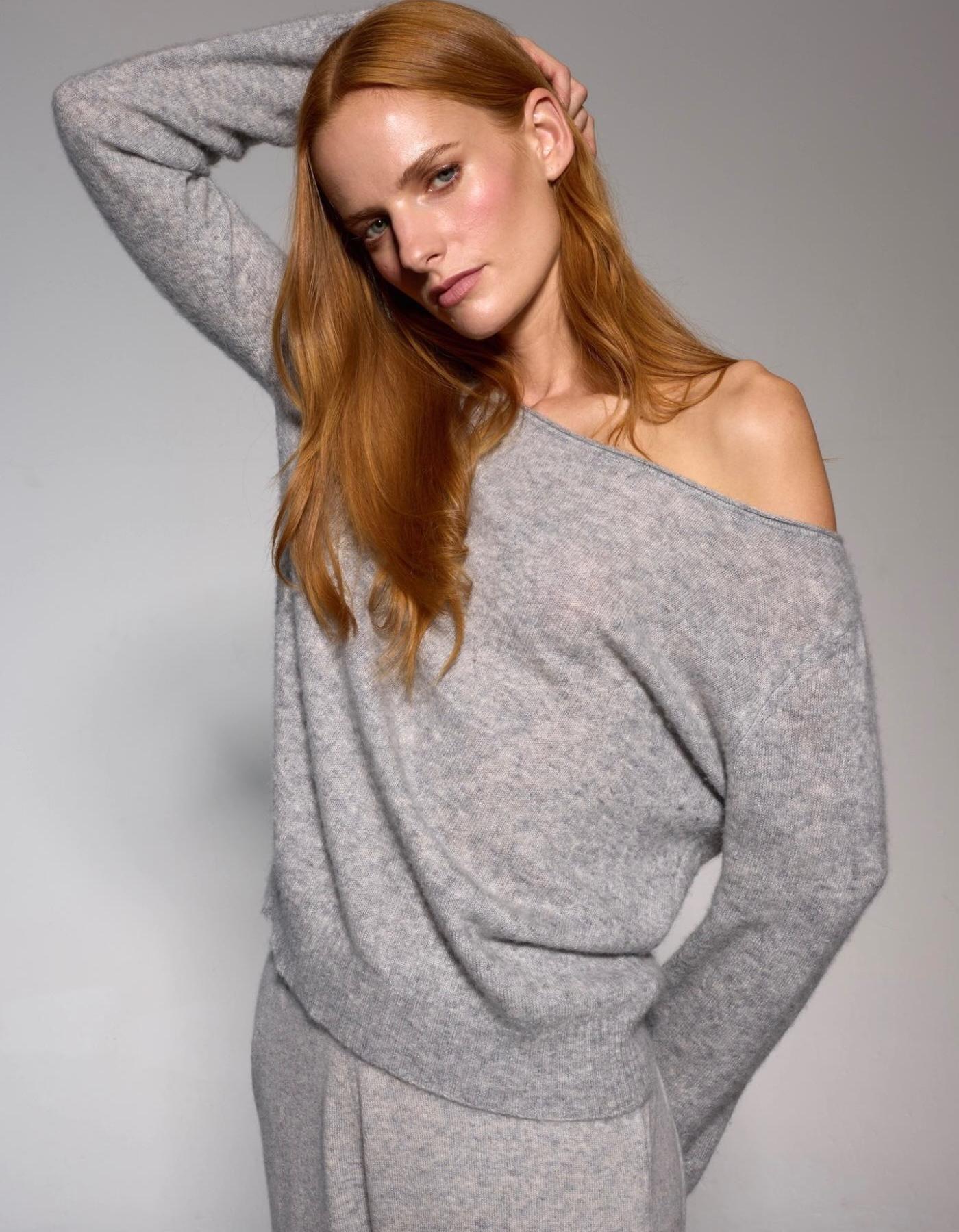 Woman wearing a gray off-shoulder sweater against a plain background
