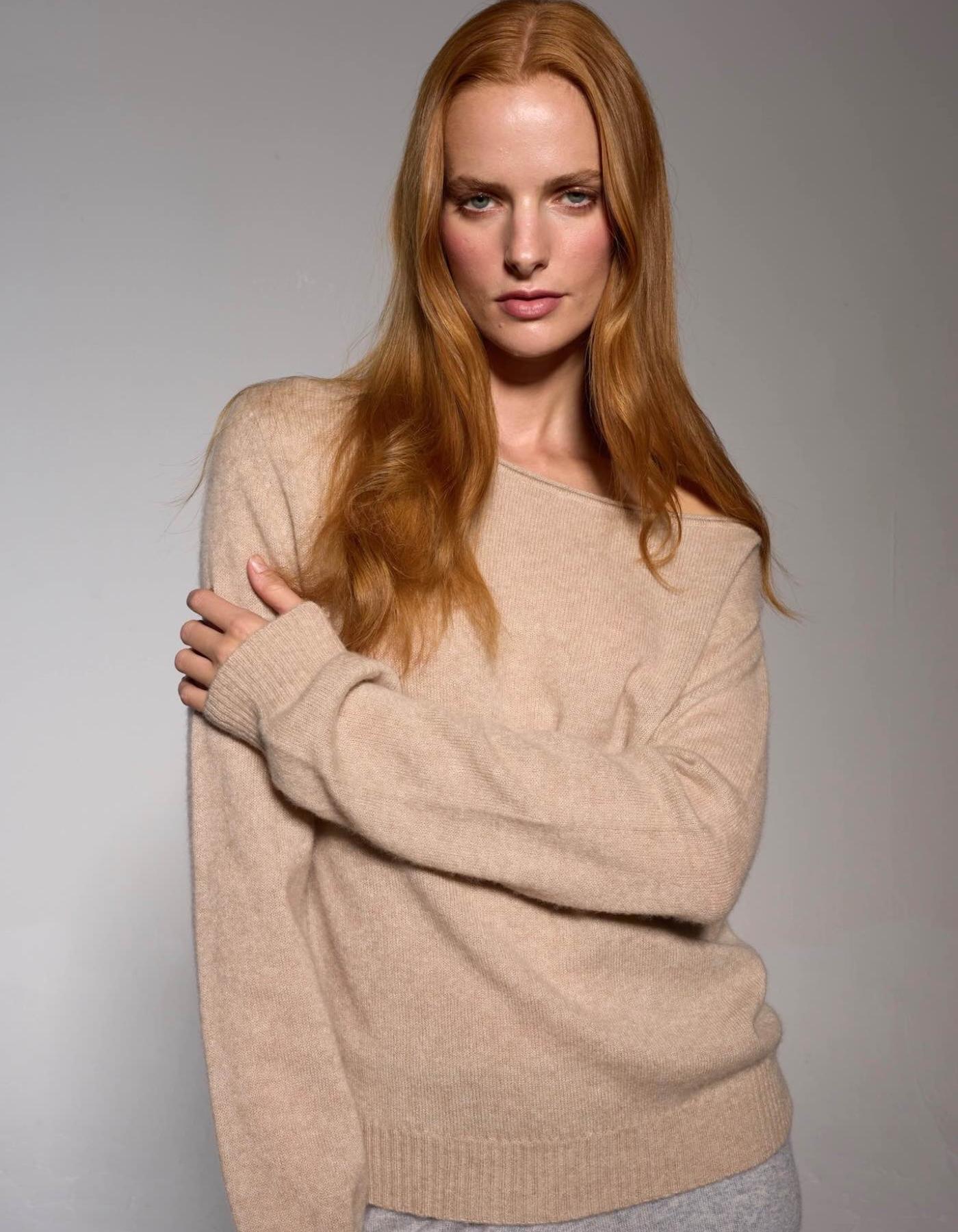 Woman wearing a beige off-the-shoulder sweater against a plain background