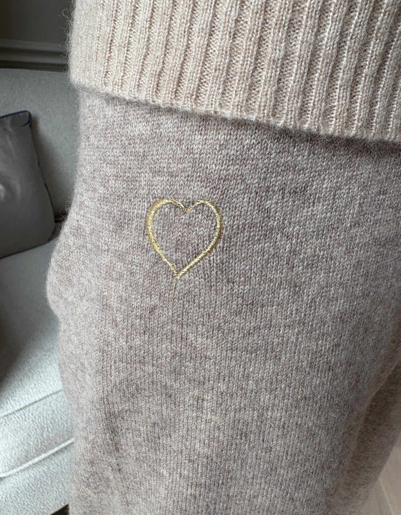 Grey joggers with a gold heart embroidery on a neutral background