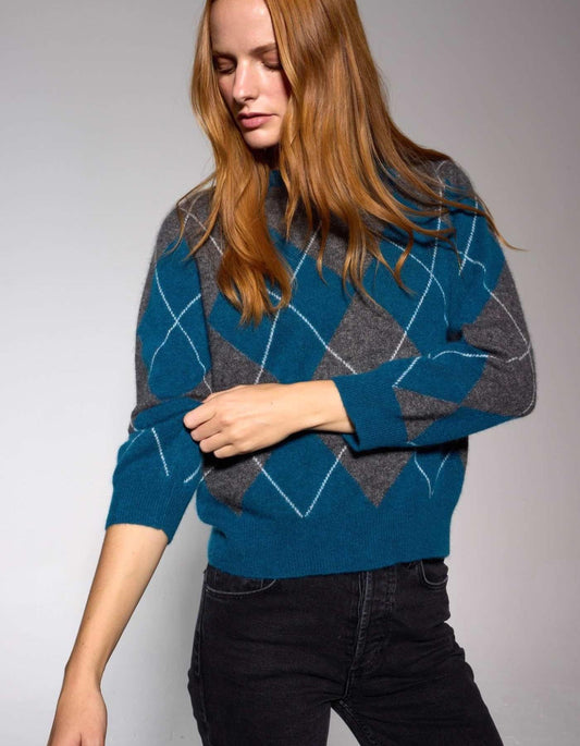 Woman wearing a blue and gray argyle patterned sweater against a plain background