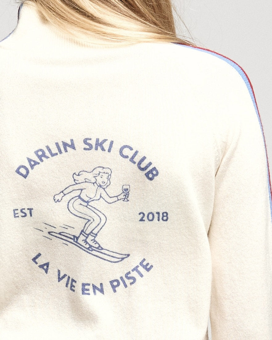 Close-up of the back of a cream-colored merino cashmere knitted jumper featuring a blue graphic print of a skier and the text 'DARLIN SKI CLUB', 'EST 2018', and 'LA VIE EN PISTE'.