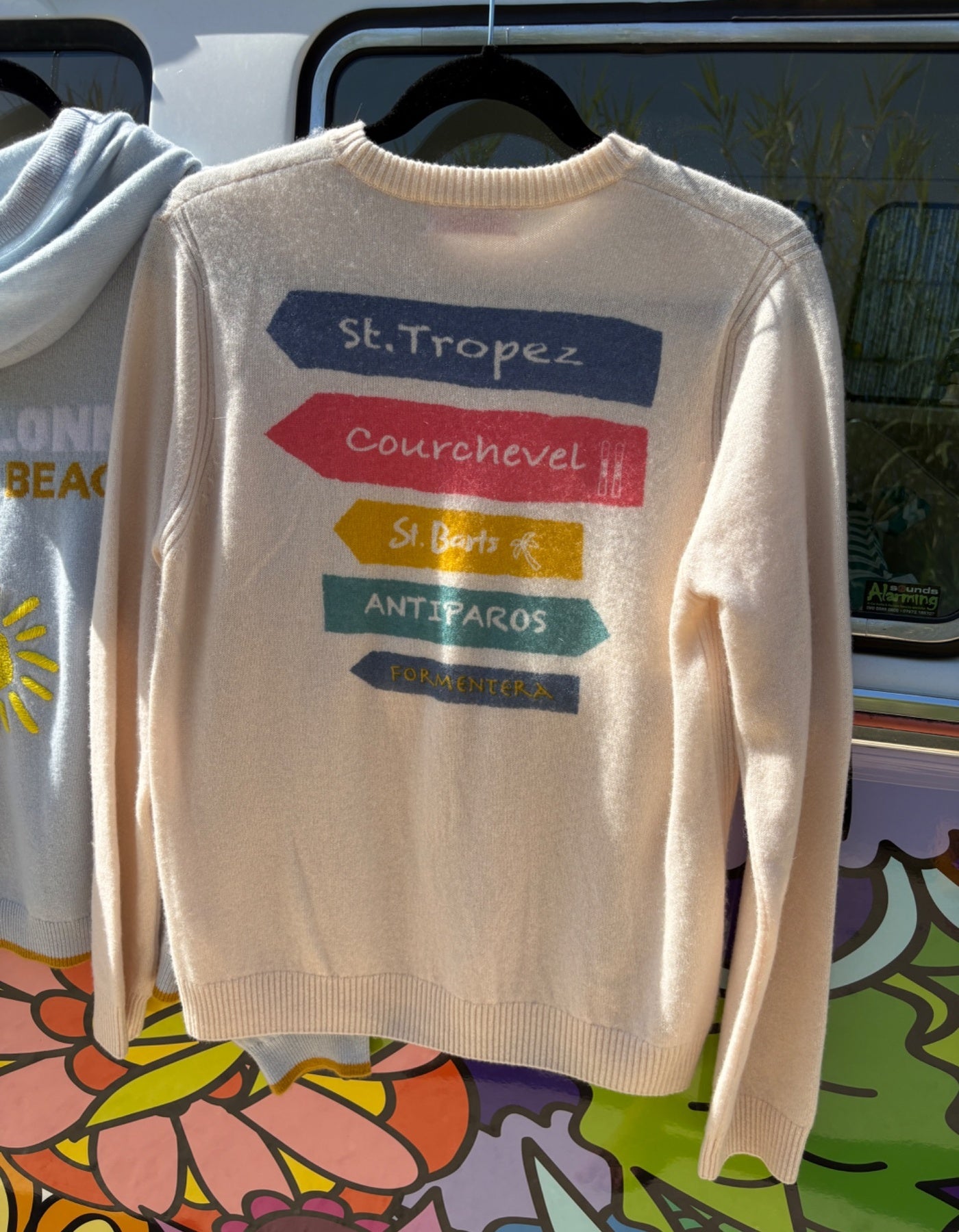 Beige sweater with colorful text on a hanger against a colorful background