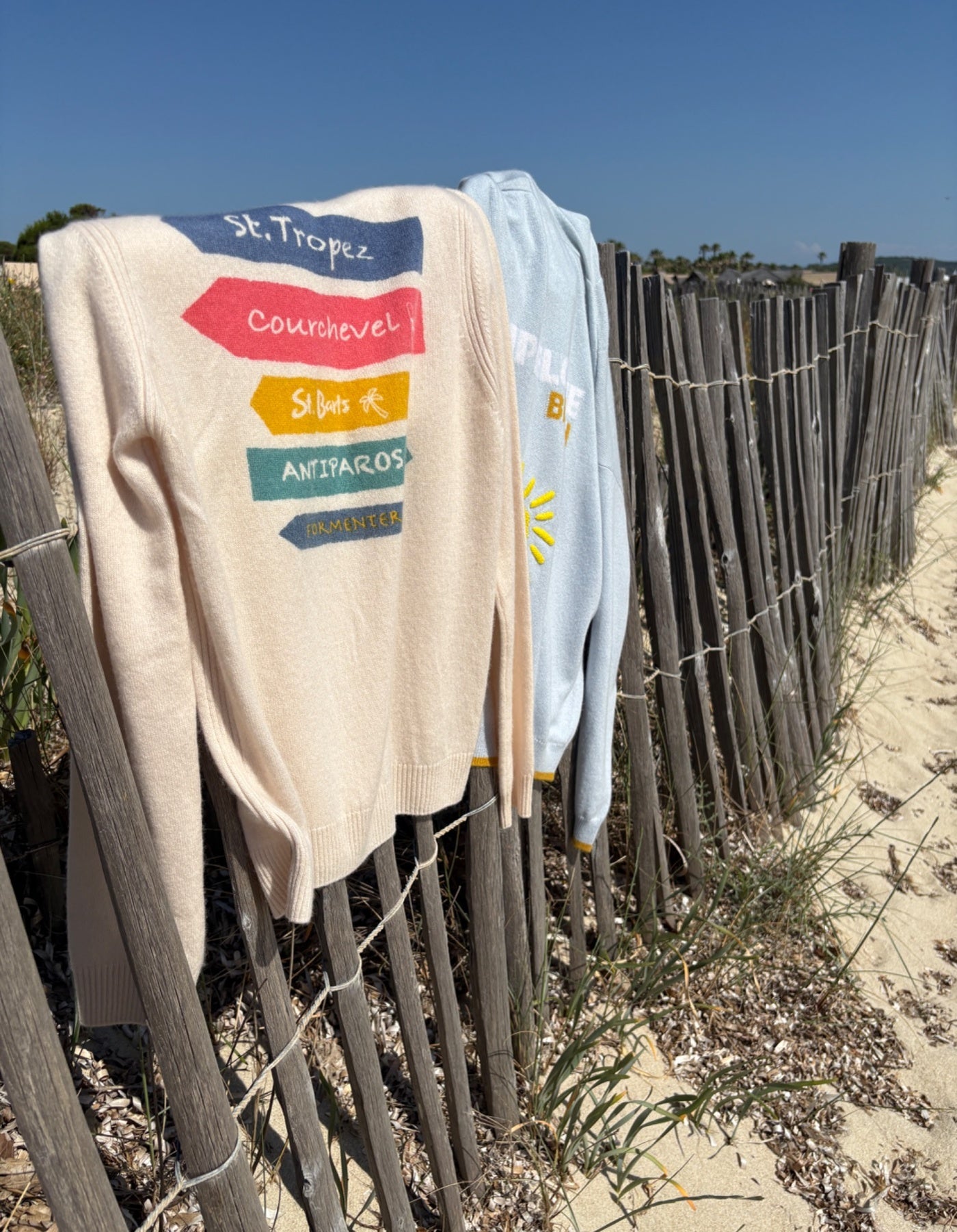 Beige jumper with colorful text and graphics on a wooden fence by the beach