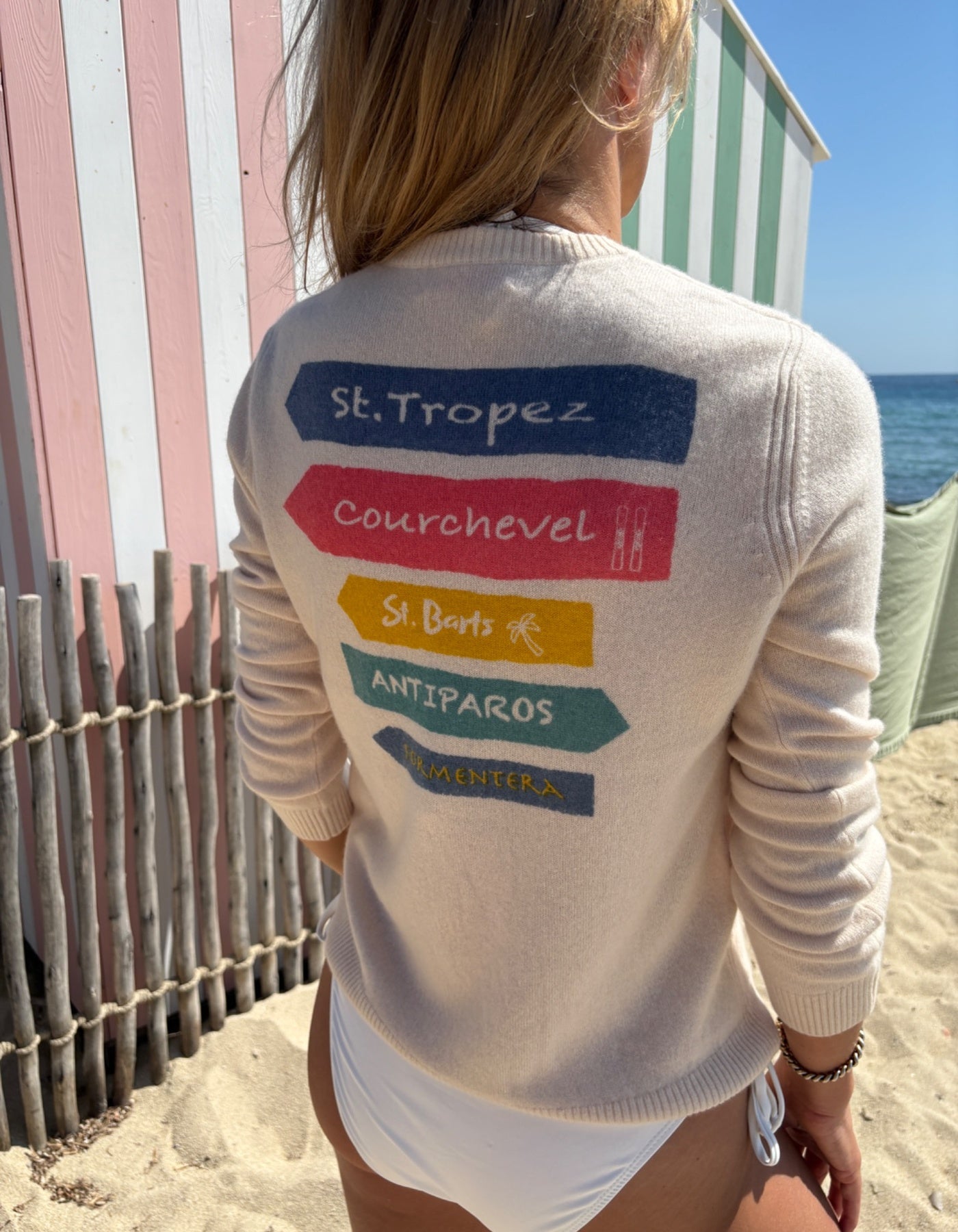 Person wearing a white cashmere jumper with colorful text on the beach