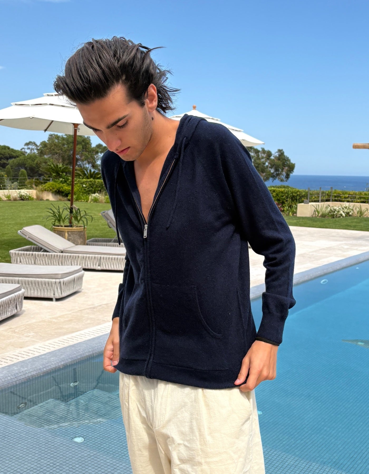 Man wearing a navy blue hoodie by a pool with a scenic background