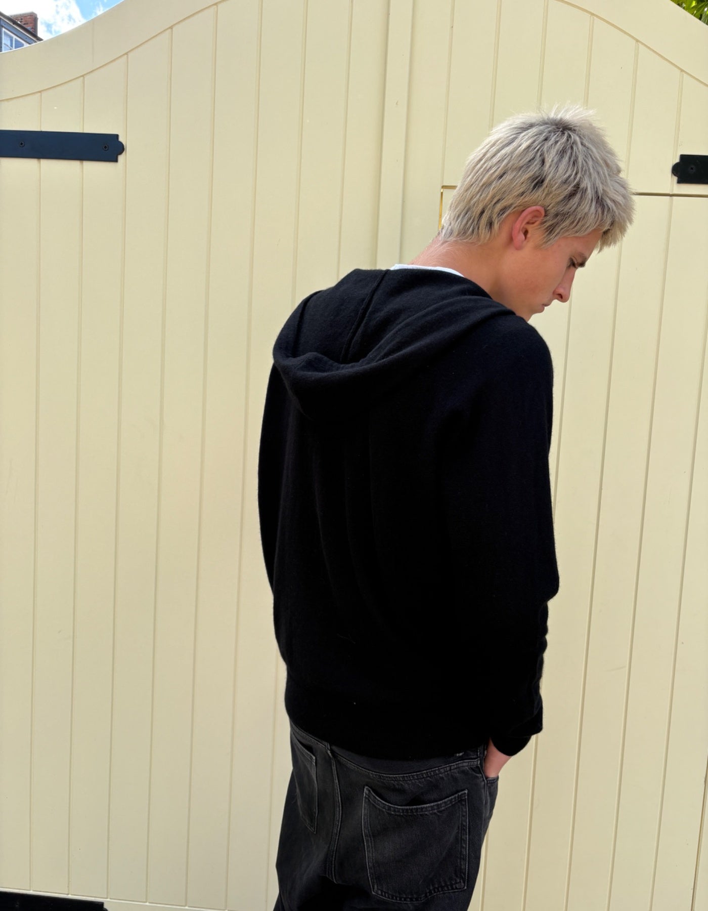 Person wearing a black hoodie standing against a beige wall.