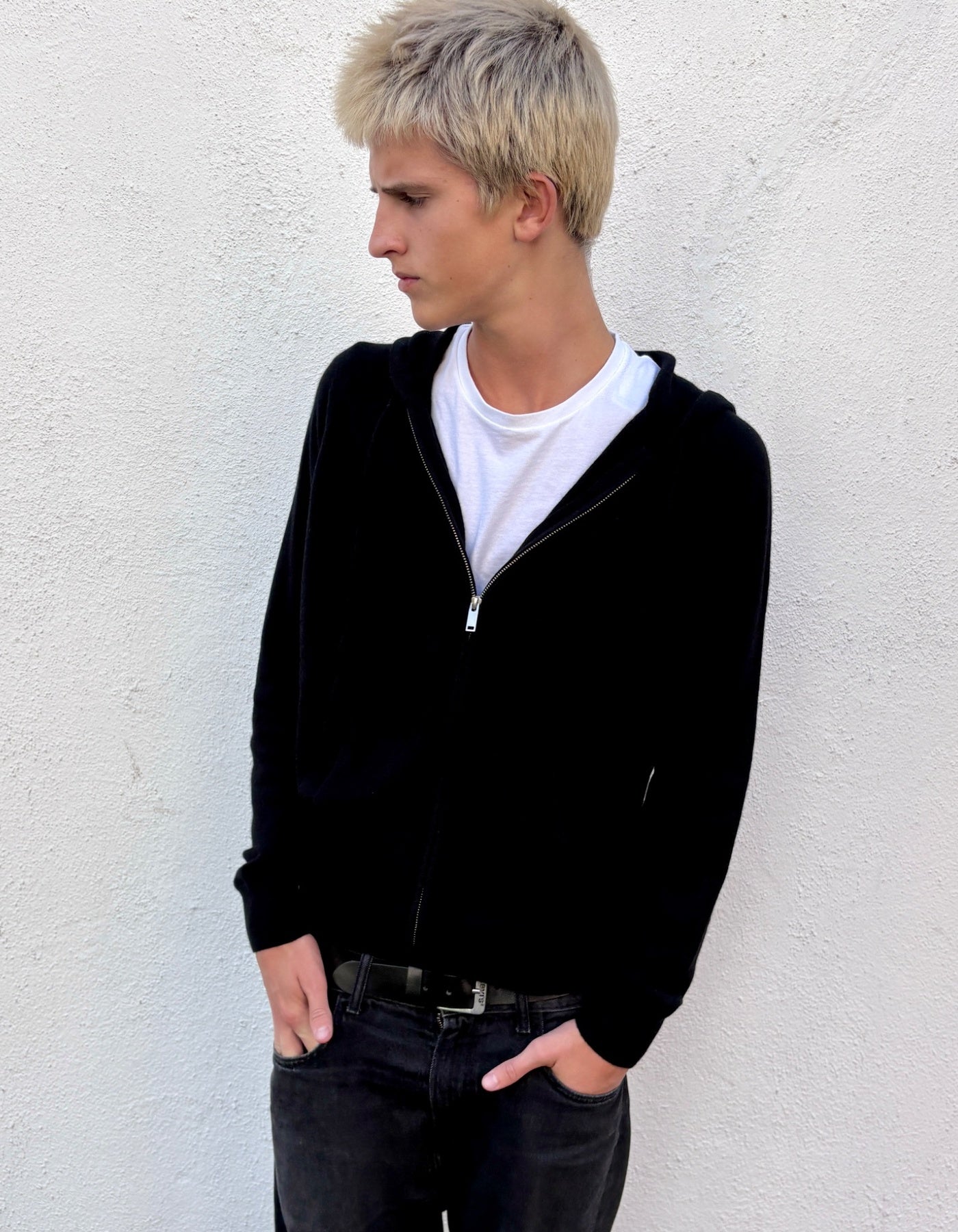Person wearing a black cashmere hoodie and white t-shirt against a light gray wall
