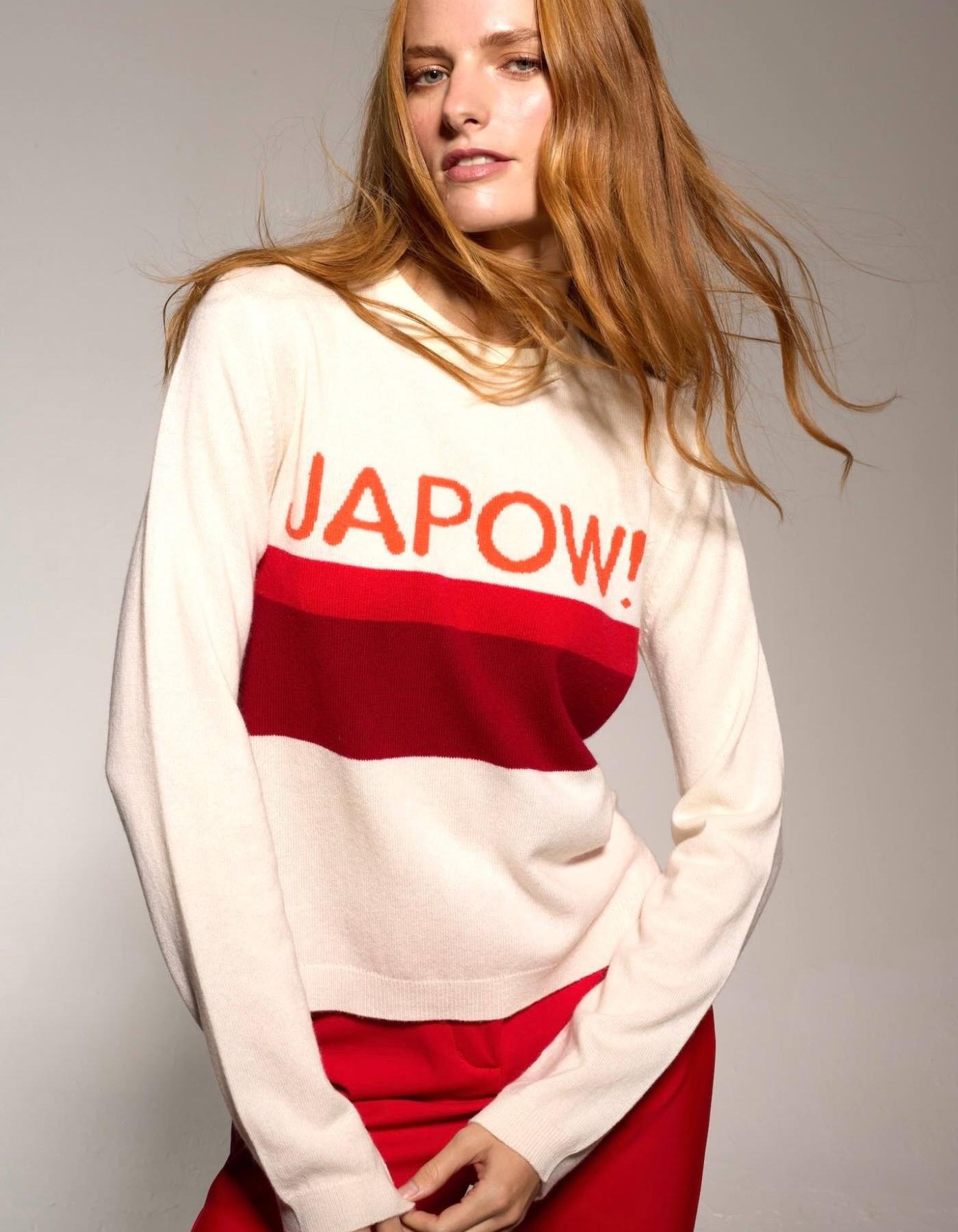 Woman wearing a sweater with 'JAPOW!' text on a plain background