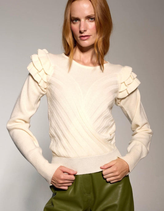 Woman wearing a cream sweater with ruffled shoulders against a grey background