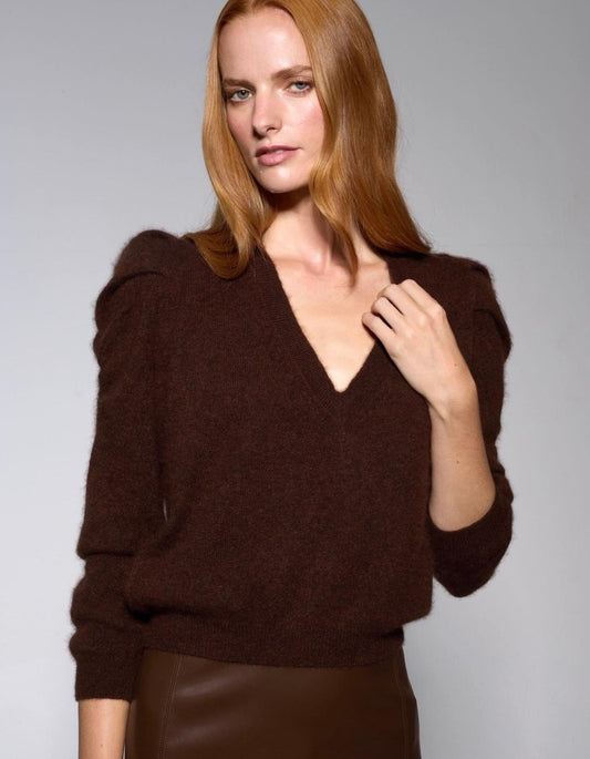 Woman wearing a brown V-neck cashmere sweater against a gray background