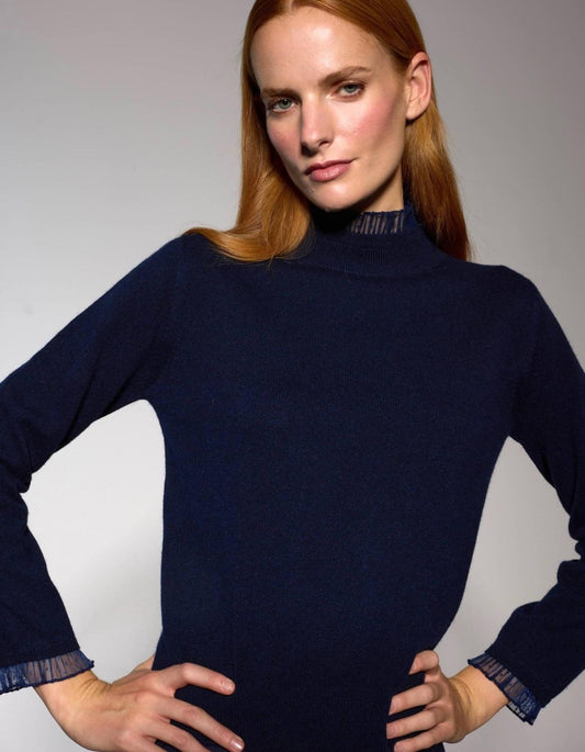 Woman wearing a navy blue lace trim turtleneck sweater against a gray background