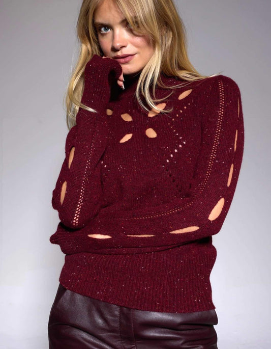 Woman wearing a burgundy sweater with cut-out design on a plain background