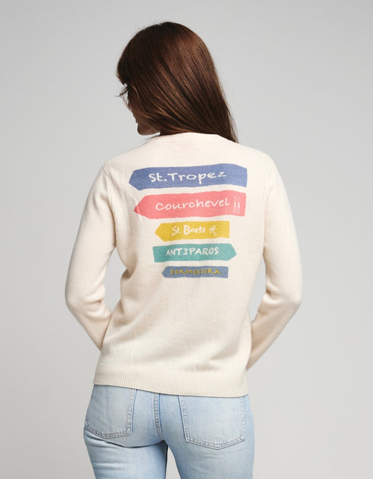 Person wearing a cream-colored sweater with colorful text on the back saying St. Tropez, Courchevel, St. Barts, Antiparos, Formentera against a white  background