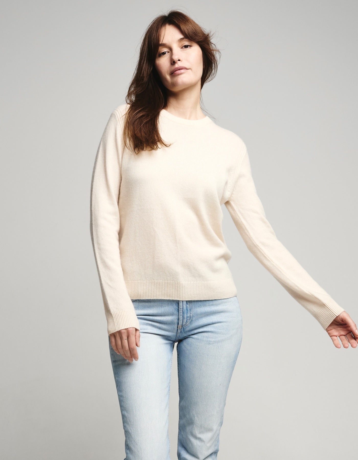 Woman wearing a cream sweater and light blue jeans on a gray background