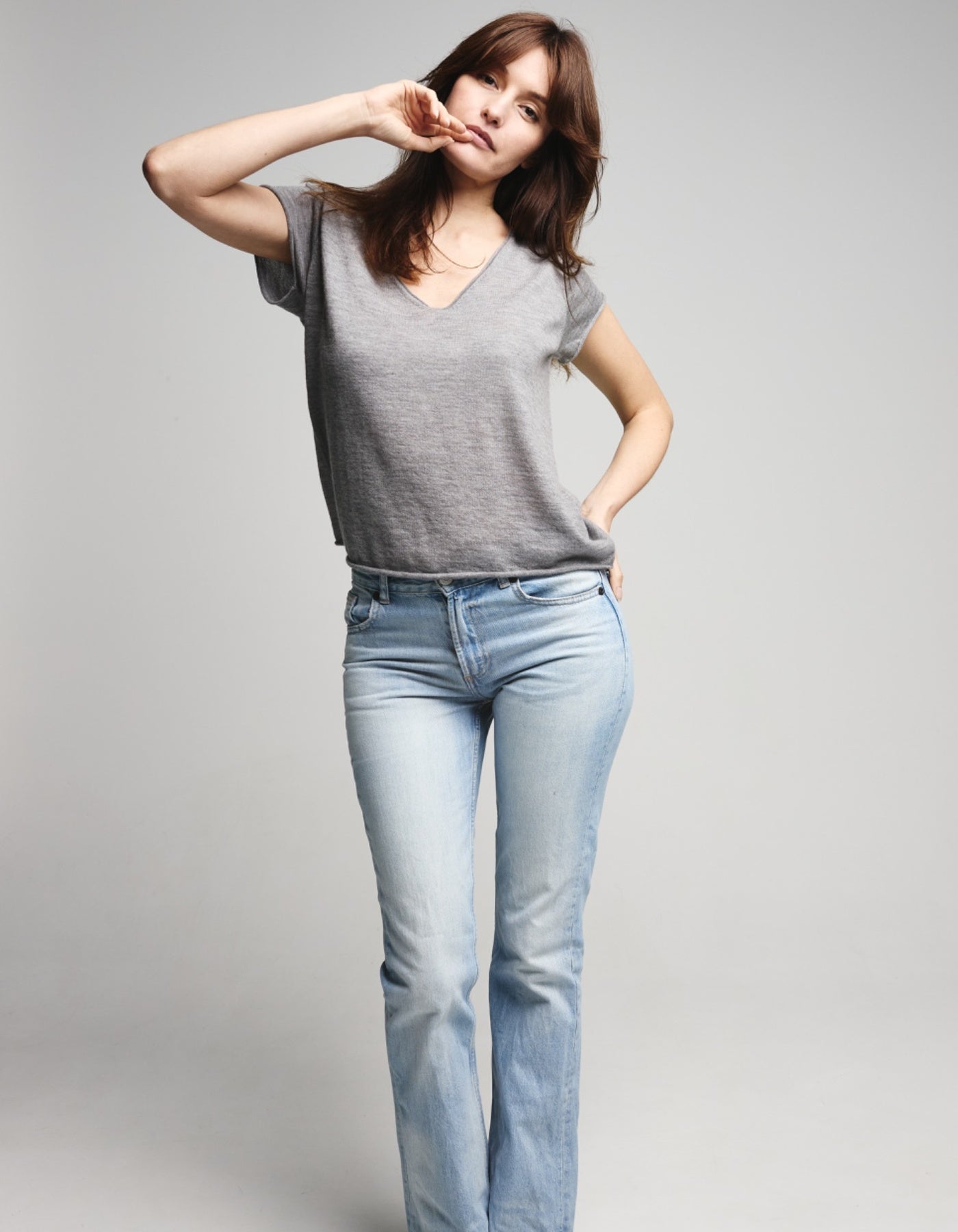 Woman wearing a gray t-shirt and light blue jeans against a plain background