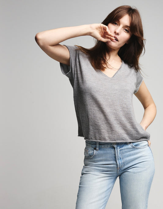 Woman wearing a gray cashmere yshirt and light blue jeans against a plain background