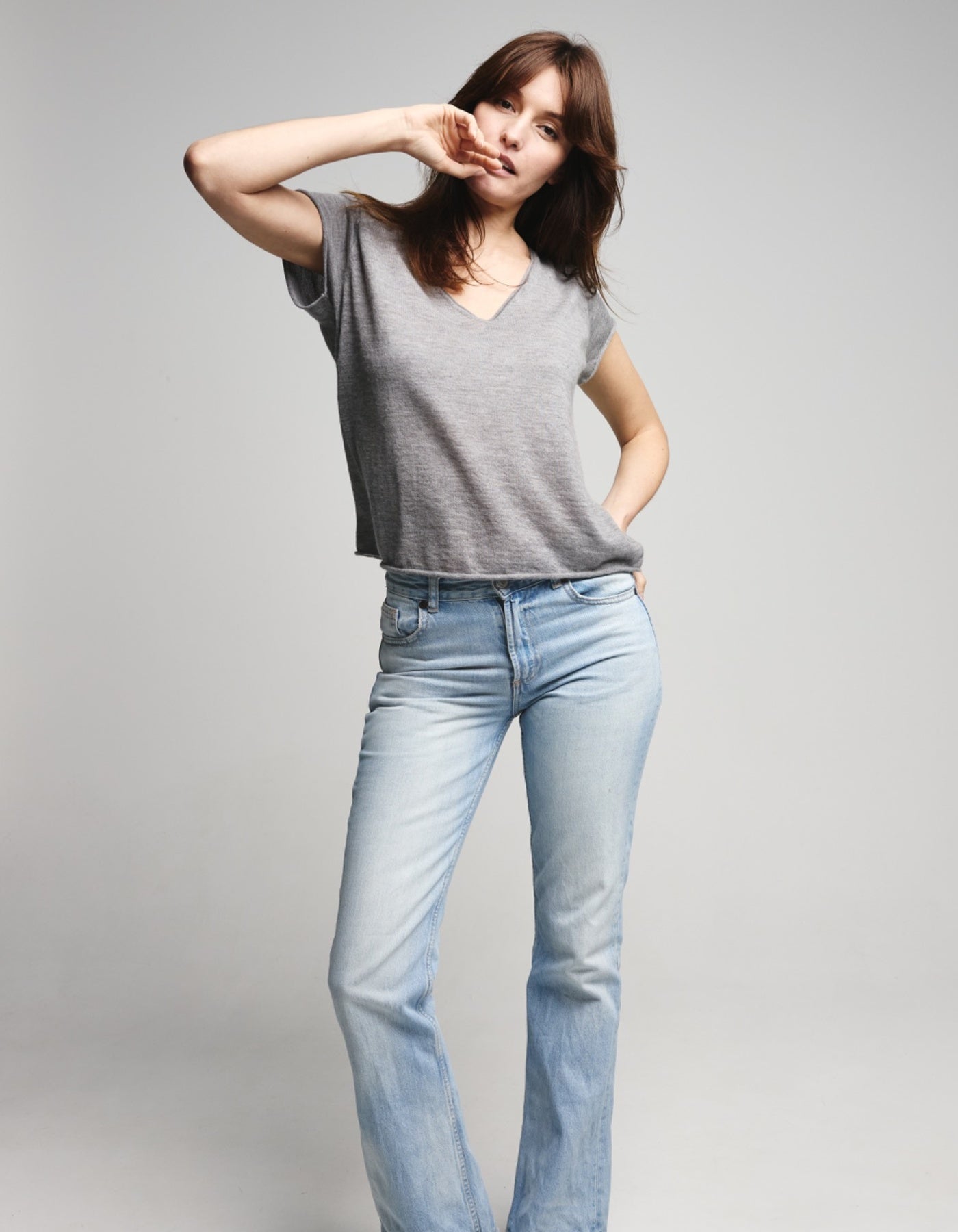 Woman wearing a gray top and light blue jeans on a plain background