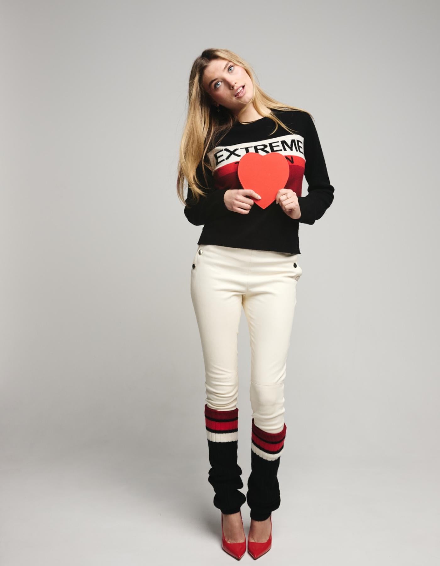 Woman wearing ski jumper with word EXTREME and 
holding a red heart-shaped object against a gray background