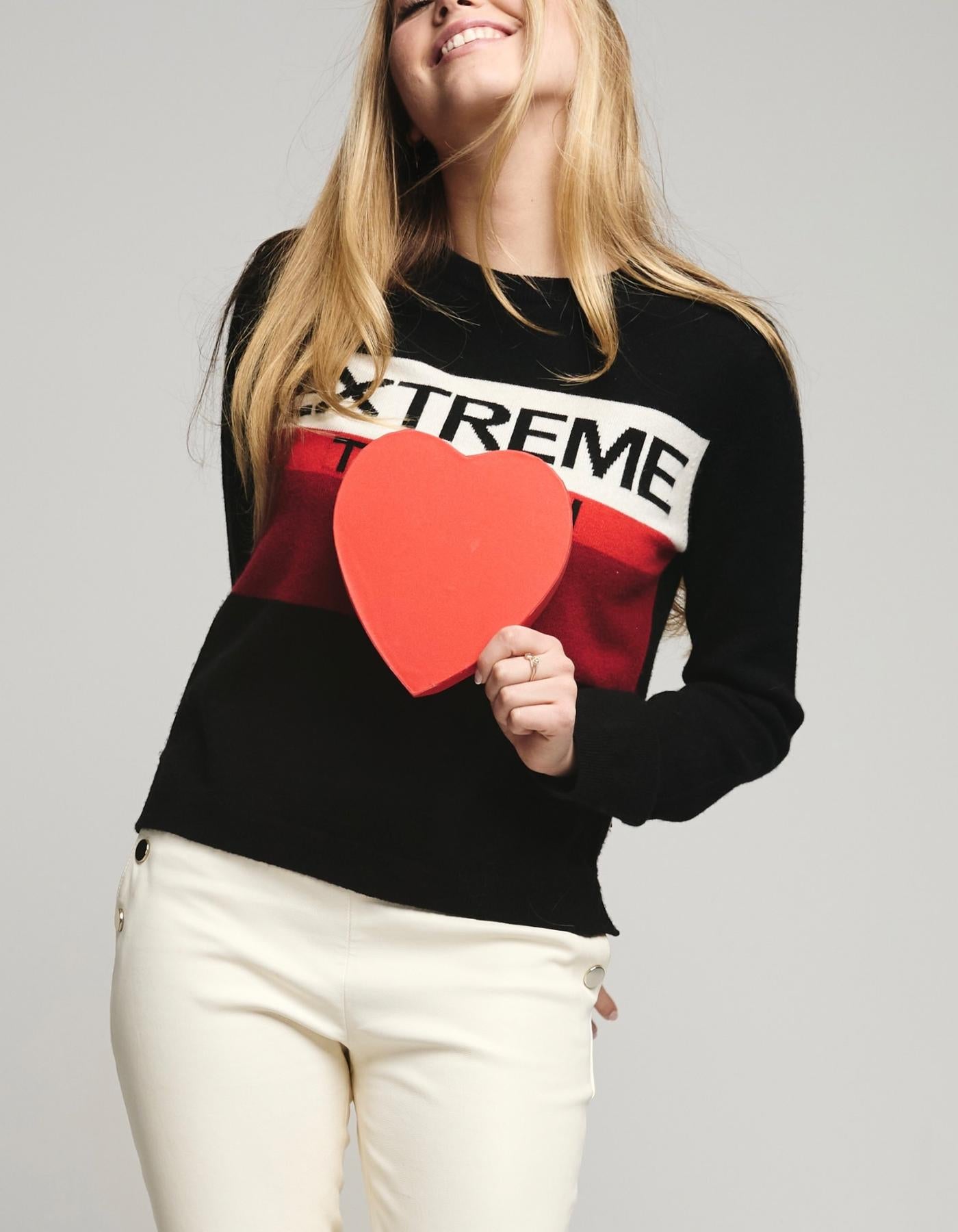 Person wearing a black sweater with a red heart and 'EXTREME' text, holding a red heart.