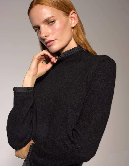 Woman wearing a black sweater with pleated collar against a plain background