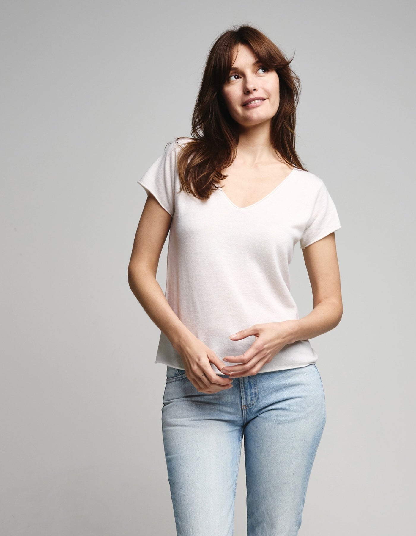 Woman wearing a white t-shirt and light blue jeans on a gray background